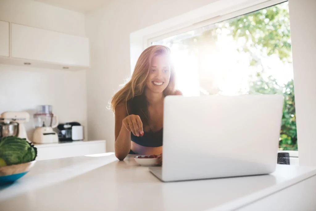 Woman smiling while working on a laptop at her kitchen counter